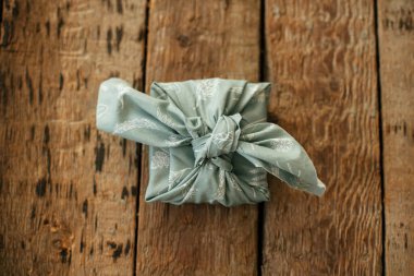 Sıfır atık hediye düz yatıyordu. Furoshiki çevre dostu basit bir hediye. Kırsal ahşap masada kumaşa sarılı şık bir Noel hediyesi. Mutlu kış tatilleri, anneler günü ya da doğum günü