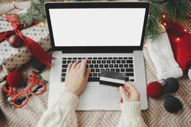 Kredi kartlı eller dizüstü bilgisayarda boş ekran, rahat yatak, şık Noel süsleri, hediye, Noel Baba şapkası. Noel satışları ve online alışveriş. Metin için boşluk
