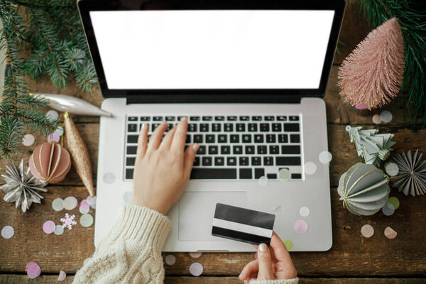 Руки с кредитной картой на ноутбуке с чистым экраном на деревенском деревянном столе со стильными рождественскими украшениями. Рождественские продажи и покупки онлайн. Вид сверху. Пространство для текста. Черная пятница