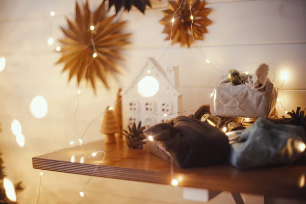 小さな家 紙の星とクリスマスの黄金のライトボケを背景に木製の棚にスタイリッシュなクリスマスプレゼント 大気中のお祝いの北欧の部屋 環境に優しいプレゼントIn Eve — ストック写真