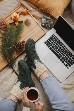 Sıcak bir fincan çayı olan kadın yumuşak yatağında dizüstü bilgisayarla, noel ışıklarıyla, yıldızlarla, çam ağacıyla, mumla ve şık bir odada yastıklarla dinleniyor. Evdeki sıcak kış tatili. Serbest çalışmak ve blog yazmak. Üst görünüm