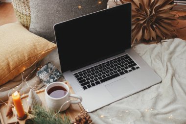 Laptop yumuşak yatakta çay, noel ışıkları, yıldızlar, çam, mum ve İskandinav odasında yastıklarla. Serbest çalışmak ve blog yazmak. Uzaktan kumanda ve çevrimiçi. Evdeki sıcak kış tatili. Boş ekran