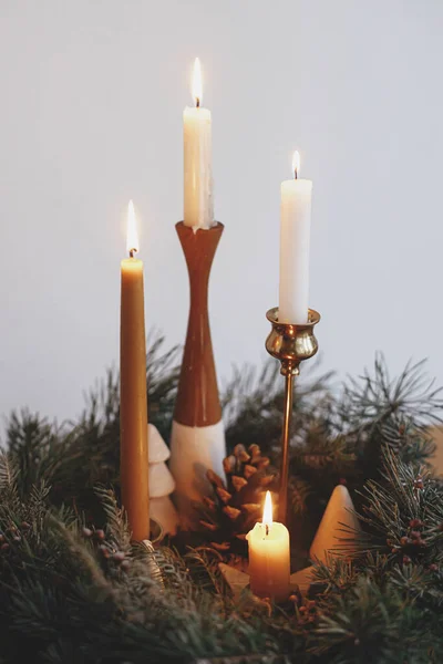 在现代喜庆的房间里 圣诞花圈里燃烧着时尚的蜡烛 花圈上有松果和装饰在白色墙壁后面的木桌上的树木 圣诞节来了大气冬季假期 — 图库照片