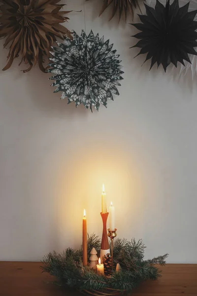 用蜡烛和装饰品装饰在白色墙壁后面的木制桌子上 上面挂满了瑞典的纸星 装饰着时尚的圣诞花环 大气冬季时间 假日的到来 丑闻性鸟类节日联欢 — 图库照片