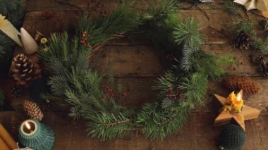 Noel çelengi yapıyorum. Eller kırmızı böğürtlen kesiyor, çam dalları düzenliyor, Noel çelenklerini köy ahşap masasında süslüyor. Üst Manzara. İyi tatiller! Atmosferik Xmas görüntüleri