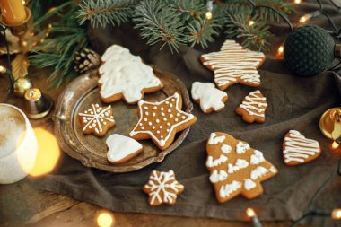 Noel kurabiyeleri, köknar dalları, peçete üzerindeki sıcak ışıklar ve kırsal ahşap masa. Huysuz atmosferik görüntü. Kış kızarıklığı. Mutlu tatiller ve mevsimler.