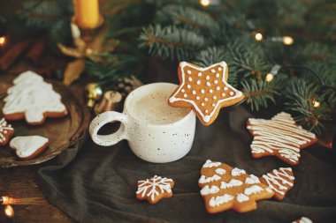 Noel kurabiyesi ve beyaz fincanda kahve, peçete ve kırsal masada köknar dalları. Kahveli Noel yıldızı kurabiyesi. Huysuz atmosferik görüntü. Kış zamanı