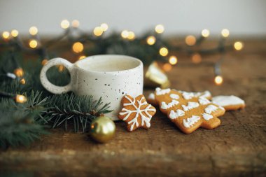 Noel kurabiyeleri, kahve fincanı, köknar dalları ve arka plandaki sıcak ışıklar rustik ahşap masa üzerinde bokeh. Huysuz atmosferik görüntü. Kış kızarıklığı. Mevsimlik selamlama, metin için boşluk