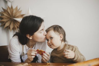 Sevimli küçük kız ve anne modern odadaki dağınık ahşap masada zencefilli kurabiye yapıyorlar. Küçük tatlı kız Noel kurabiyeleri yapmaya yardım ediyor. Anne kız güzel anlar.