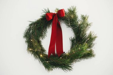 Kırmızı kurdeleli ve beyaz duvarında altın ışıklar asılı şık bir Noel çelengi. Mutlu Noeller ve mutlu tatiller! Çam dalları ve beyaz üzerine izole kırmızı kurdele ile basit geleneksel xmas çelengi