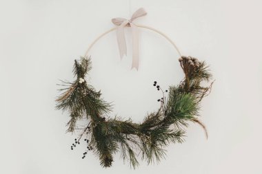 Beyaz arka planda asılı modern noel çelengi. Atmosferik zaman. Minimalist Xmas boho çelengi, otlar ve şeritlerle, beyaza izole edilmiş. Mutlu Noeller ve mutlu tatiller!