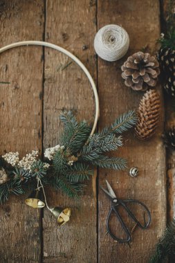 Modern noel çelengi, kırsal düzlük. Minimalist Xmas boho çelengi, çan, çam kozalakları, iplik, kırsal masada makas. Atmosferik karamsar görüntü. Mutlu Noeller.!