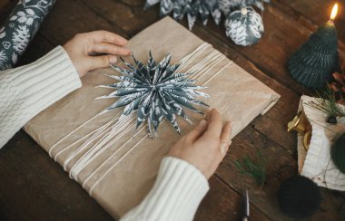 Noel hediyesi paketleme, atmosferik görüntü. Kırsal masa zemininde makas, mum ve süslemelerle mavi kâğıt yıldızlı el yapımı Xmas hediyeleri. Mutlu Noeller.