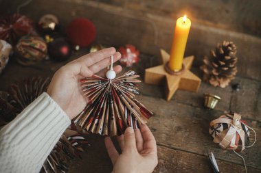 El yapımı Noel meleği kırmızı ambalaj kağıdından kağıt kaplı, arka planda kağıt yıldızlı, mumlu ahşap masa. Atmosferik karamsar görüntü. Mutlu Noeller ve mutlu tatiller!