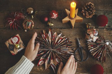 Mutlu Noeller! Kırsal ahşap masa üzerinde kırmızı el işi ambalaj kağıdından yapılmış şık bir Noel yıldızını tutan eller. Atmosferik karamsar görüntü. El yapımı şenlik dekorasyonu, tatil hazırlığı
