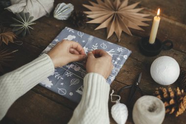 Sıfır noel hediyesi. Noel hediyesini kırsal ahşap masaya makas, kağıt yıldız, mum ile saran eller. Atmosferik karamsar zaman, kuzey tarzı. İyi tatiller.!