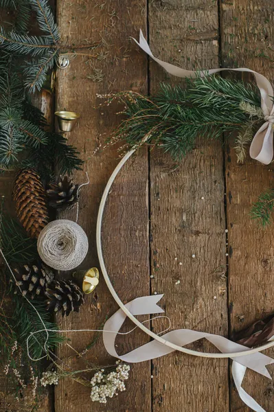 Modern christmas wreath flat lay on rustic wooden background. Boho wreath on rustic table with ribbons, thread, herbs, pine cones. Atmospheric image. Winter holiday preparation