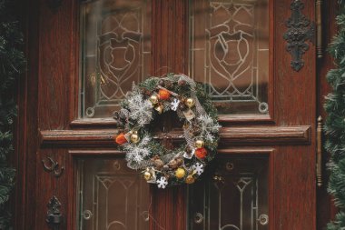Eski ahşap kapılarda kahverengi süsler ve kar taneleri olan modern Noel çelenkleri. Avrupa şehir caddesinde kış tatili için Noel dekorasyonu. Mutlu Noeller.!
