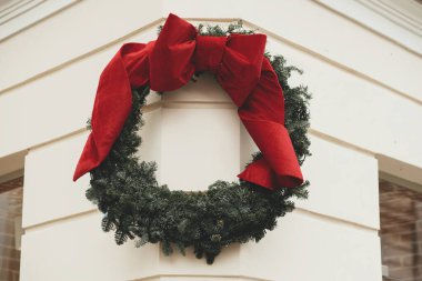 Eski bina duvarında büyük kırmızı bir fiyonk olan modern Noel çelengi. Avrupa şehir caddesinde kış tatili için Noel dekorasyonu. Mutlu Noeller.!