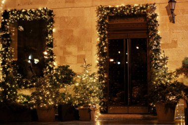 Şık noel ladin dalları ve altın ışıklarıyla aydınlatılmış ağaçlar akşam bina kapısını aydınlatıyor. Atmosferik sihir zamanı. Kış tatilleri için Noel dekorasyonu. Mutlu Noeller.!
