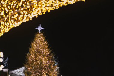 Parlak yıldızlı şık bir Noel ağacı ve akşam vakti gökyüzünde altın ışıklar. Atmosferik sihir zamanı. Avrupa şehir meydanı ve tatil fuarının Noel dekoru. Mutlu Noeller.!