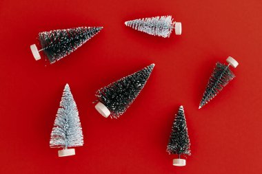 Noel yatağı. Kırmızı arka planda şık küçük noel ağaçları kompozisyonu. Modern minimalist tebrik kartı. Mutlu Noeller ve mutlu yıllar! Minimum xmas düzlüğü