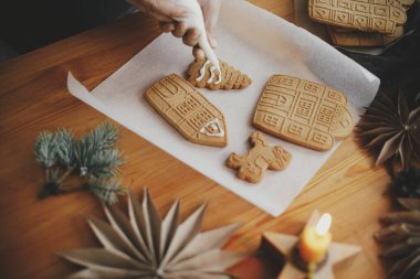 Noel kurabiyelerini ahşap masaya mum, ladin dalı ve kağıt yıldızlarla süsleyen bir kadın. Üst Manzara. Zencefilli ekmek evi yapıyorum. Noel tatili hazırlığı ve geleneği