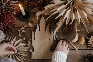 Şık Noel yıldızları yapmak. El yapımı kağıt torbadan yıldız kesen eller, arka planda İsveç yıldızları, iplik, mum, kırsal kesimde makas. Festival dekorunun en üst görünüm süreci