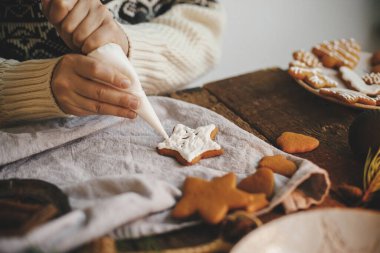 Eller zencefilli kurabiye yıldızını kırsal masada süsleyerek süslüyor. Atmosferik karamsar görüntü. Geleneksel zencefilli kurabiye yapan kadın