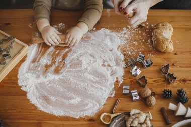 Tatlı bir kız bebek, annesiyle birlikte zencefilli kurabiye için hamur yoğuruyor, elleri kapalı. Karmaşık masa üstü manzarası. Küçük tatlı kız Noel kurabiyeleri yapmaya yardım ediyor. Özgün anlar