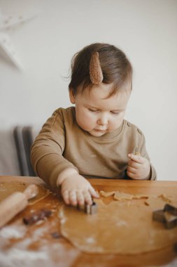 Sevimli küçük kız, Noel kurabiyelerini ahşap masada birlikte yapıyor. Sevimli küçük kız, annesinin kurabiye için hamuru şenlikli makaslarla kesmesine yardım ediyor. Aile zamanı.