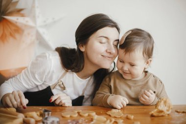 Sevimli küçük kız ve anne modern odadaki dağınık ahşap masada zencefilli kurabiye yapıyorlar. Küçük tatlı kız Noel kurabiyeleri yapmaya yardım ediyor. Anne kız güzel anlar.