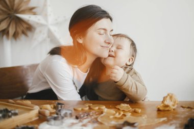 Sevgili anne-kız anları, mutlu aile anları. Sevimli küçük kız ve anne Noel kurabiyesi yapıyorlar. Mutlu anne, küçük kızına sarılıyor. Tatil hazırlığı