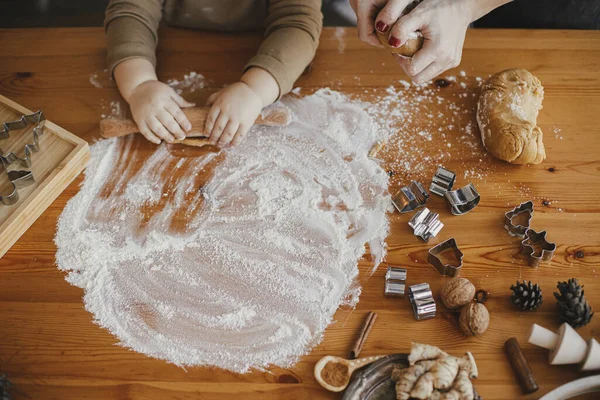 Tatlı bir kız bebek, annesiyle birlikte zencefilli kurabiye için hamur yoğuruyor, elleri kapalı. Karmaşık masa üstü manzarası. Küçük tatlı kız Noel kurabiyeleri yapmaya yardım ediyor. Özgün anlar