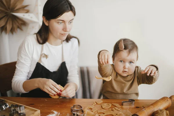 現代的な装飾されたスカンディナヴィアの部屋で木製のテーブルの上にジンジャーブレッドクッキーを作る母親と一緒に愛らしい赤ちゃんの娘 クリスマスクッキーとかわいい面白い幼児の女の子 ママ娘の瞬間 — ストック写真