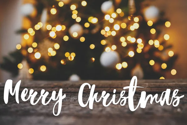 メリークリスマスグリーティングカード クリスマスツリーに対する素朴な木のメリークリスマステキストは黄金のボケを点灯します 大気中のクリスマス前夜 ハッピー ホリデー 手書きのサイン — ストック写真