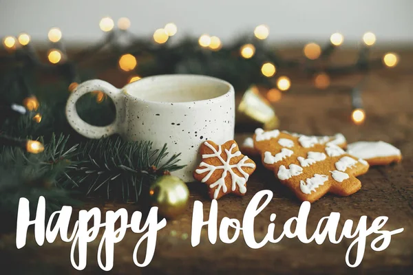 クリスマスジンジャーブレッドクッキー コーヒーカップ モミの枝 素朴なテーブルの上のライトに幸せな休日のテキスト シーズンの挨拶カード 手書きのサインだ メリークリスマス — ストック写真