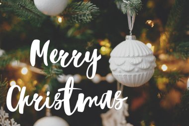Mutlu Noeller tebrik kartı. Modern beyaz mücevher üzerine mutlu noel metinleri ışıklarla süslü boho noel ağacında asılı. Seasons selamı. İyi tatiller! El yazısı işareti