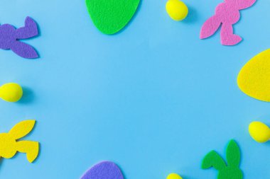 Colorful Easter bunnies and eggs frame on blue background, flat lay with space for text. Happy Easter! Purple, pink, yellow artificial bunny and egg decor. Creative Easter hunt concept