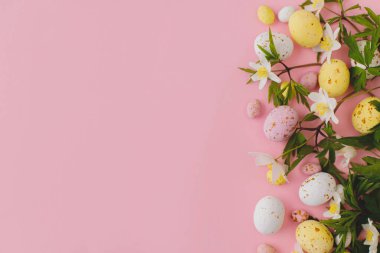 Colorful Easter chocolate eggs and spring flowers border flat lay on pink background. Stylish easter background and greeting card. Happy Easter!