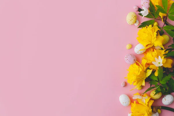 カラフルなイースターチョコレートの卵と水仙の花の境界線ピンクの背景に ハッピーイースター スタイリッシュなイースターフラットレイアウト グリーティングカードまたはバナーテンプレート — ストック写真