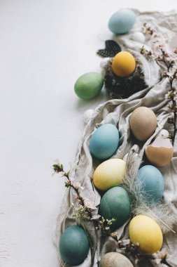 Mutlu Paskalyalar! Şık bir kırsal Paskalya düzlüğü ve yazı için yeri vardı. Doğal boyanmış renkli yumurtalar, kiraz çiçekleri, tüyler ve beyaz kırsal masadaki keten kumaş üzerindeki yuva kompozisyonu. Tebrik kartı