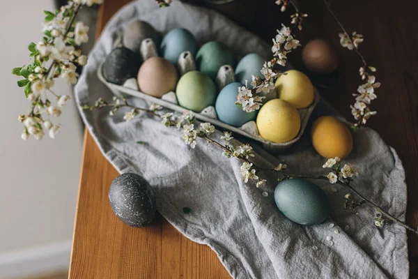 复活节快乐 复活节彩蛋放在带有樱花的乡村餐桌上 在木制板上的纸盘上 用亚麻布餐巾和春花把彩蛋自然染成彩色 乡村静谧的生活 — 图库照片