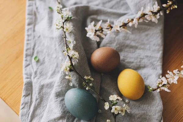 复活节快乐 复活节彩蛋放在带有樱花的乡村餐桌上 色彩艳丽的彩蛋在亚麻布餐巾和春花的顶部尽收眼底 乡村静谧的生活 大气图像 — 图库照片