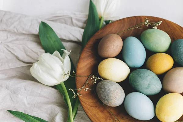 精美的复活节彩蛋 木制盘子 郁金香和亚麻布餐巾 放在乡村的白色桌子上 复活节快乐 天然色彩艳丽的彩蛋与春花的乡村组合 — 图库照片