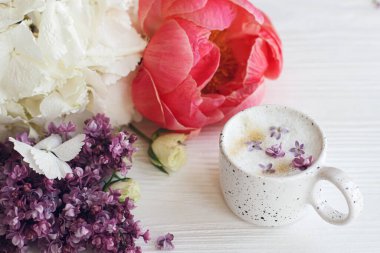 Güzel şakayık, leylak, gül çiçekleri, şık bir fincan kahve. Anneler Günün kutlu olsun. İyi sabahlar. Leylak yapraklı lezzetli kahve ve beyaz ahşap arka planda şık bir buket.