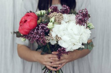 Güzel şakayık, leylak, gül, ortanca çiçeği ve okaliptüs buketi tutan kırsal giysili bir kadın. Modern düğün buketi ellerde. Anneler günün kutlu olsun ya da sevgililer günün kutlu olsun