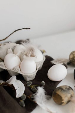 Paskalya 'nın stil sahibi sakin yaşamı. Tepside doğal yumurtalar, tüyler, söğüt dalları beyaz ahşap masada sade keten peçete. Basit kırsal Paskalya estetiği Pastel beyaz ve kahverengi renklerde