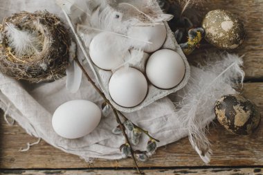 Paskalya kırsalındaki şık hayat. Tepside doğal paskalya yumurtaları, tüyler, söğüt dalları, yuva, eski ahşap masa üzerinde keten kumaş, düz yatak. Mutlu Paskalyalar! Basit kırsal estetik.