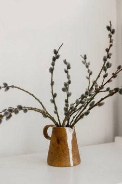 Willow branches in stylish rustic vase on wooden table. Modern Easter still life. Pussy willow branches in home, natural spring decor. Simple Easter rural minimal aesthetics. Space for text